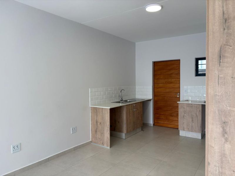 A clean, modern kitchen area featuring light wood cabinetry, subway tile backsplash, stainless steel sink, and neutral floor tiles.