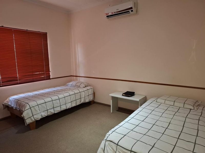 A functional bedroom featuring carpeted flooring, a wall-mounted air conditioning unit, and venetian blinds.