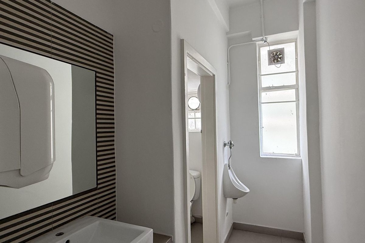 A functional office bathroom featuring a wall-mounted basin, a wall-mounted urinal, and a tiled feature wall with a mirror.