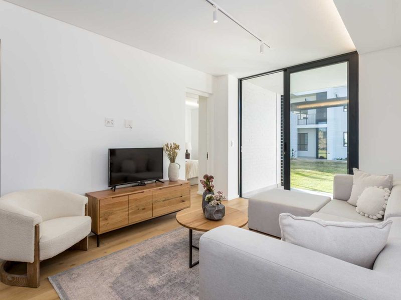 A bright and modern living room featuring hardwood flooring, track lighting, and large sliding glass doors that provide access to the outdoor area.