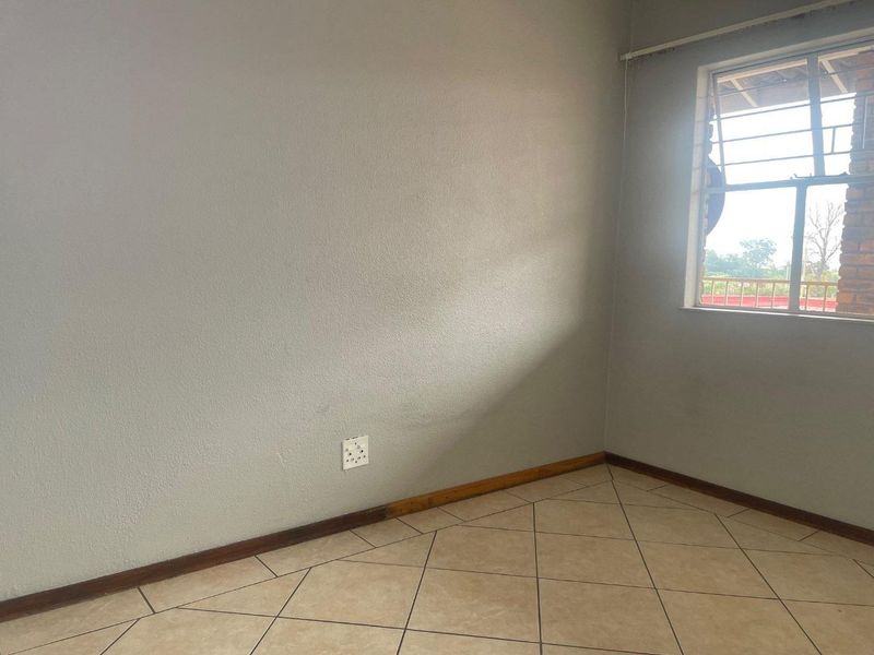 An empty bedroom featuring neutral tiled flooring, a window with security bars, and standard electrical fixtures, ready for personalization.