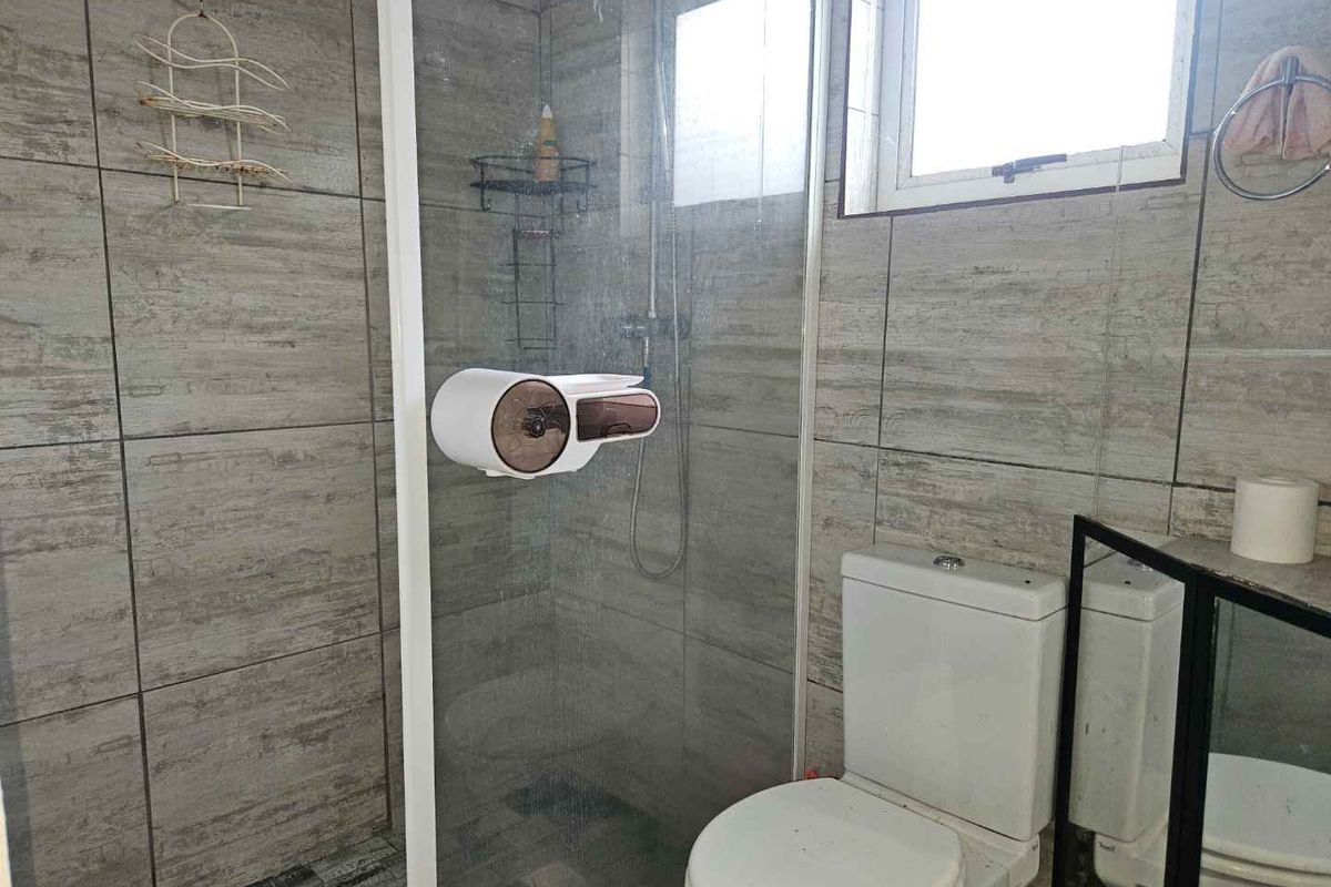 A functional bathroom featuring floor-to-ceiling grey tiled walls, a glass-enclosed shower, and a standard white toilet suite.
