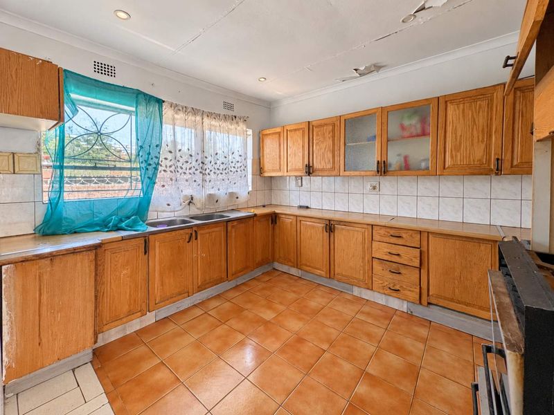 A dated kitchen featuring wooden cabinetry, tiled flooring, and a double basin sink, requiring cosmetic updates to modernize the space.