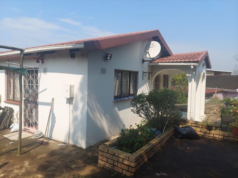 Rear view of the house featuring a covered patio, brick planter box, and tiled roof structure.