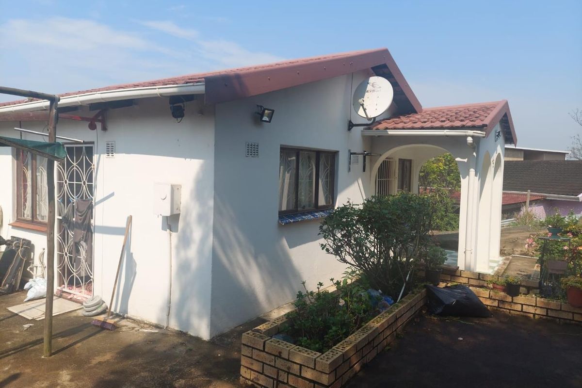 Rear view of the house featuring a covered patio, brick planter box, and tiled roof structure.