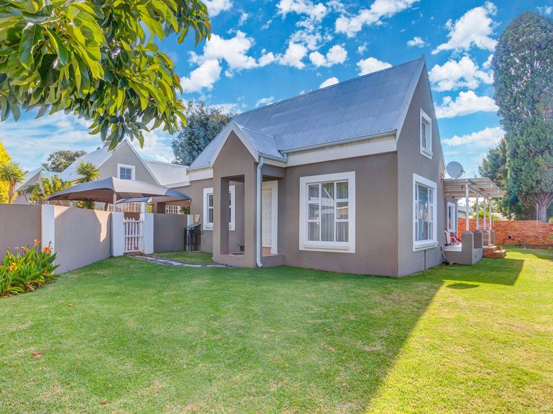A well-maintained residential property featuring a plastered exterior, corrugated metal roof, and a neatly landscaped front garden with a paved entrance path.