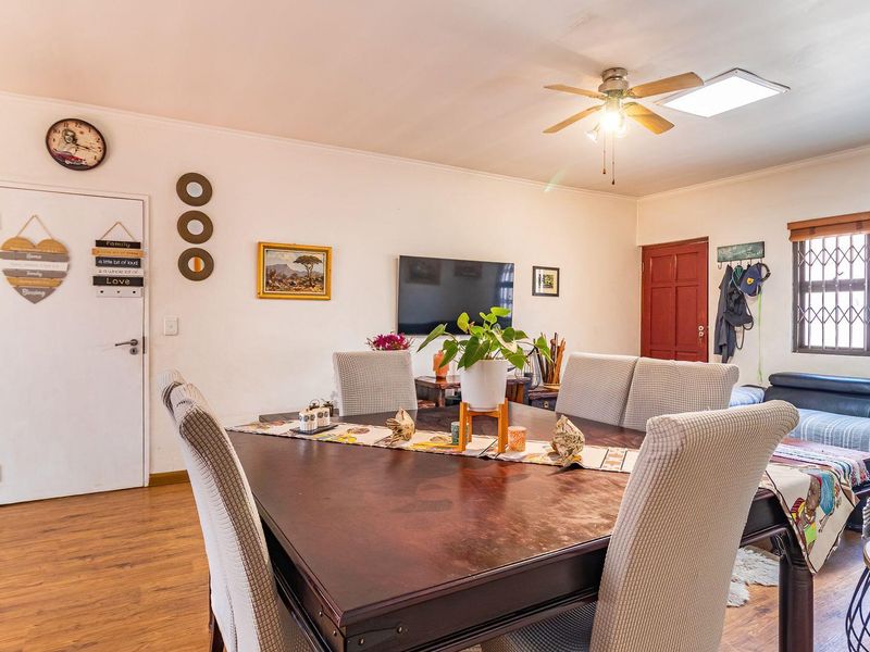 Open plan living and dining area featuring laminate flooring, a ceiling fan, and security gate access, providing a functional and versatile living space.