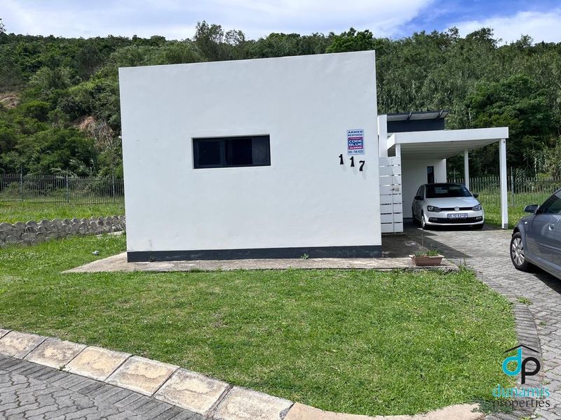 Front view of a modern residential property featuring a clean white facade, a paved driveway with a carport, and established perimeter fencing.
