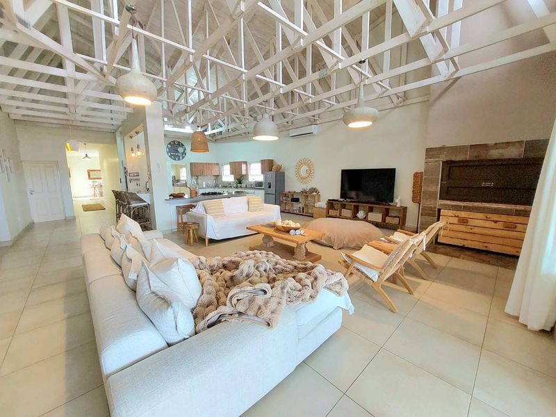 Spacious open-plan living area featuring a high vaulted exposed truss ceiling, tiled flooring, and an integrated kitchen with breakfast bar.