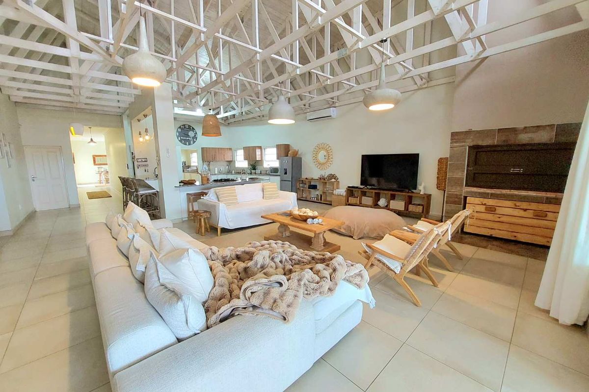 Spacious open-plan living area featuring a high vaulted exposed truss ceiling, tiled flooring, and an integrated kitchen with breakfast bar.