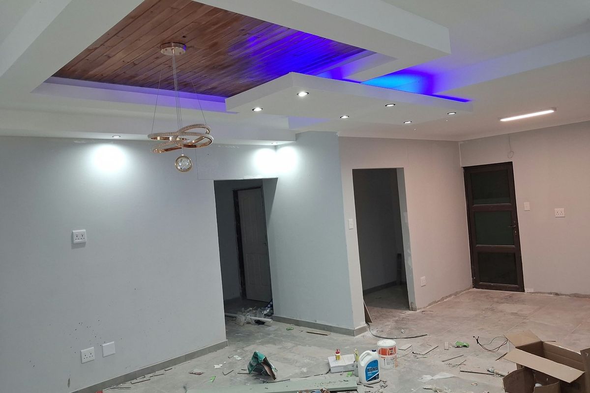 Living area under construction featuring a modern recessed ceiling with timber inlay and integrated LED lighting, awaiting final flooring and finishing touches.