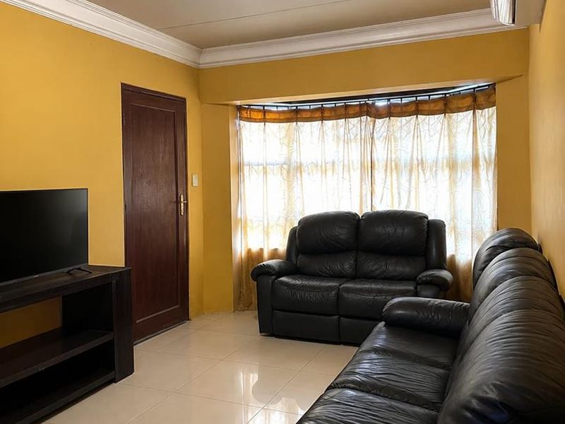 A living room featuring tiled flooring, a bay window, and a wall-mounted split-system air conditioner.