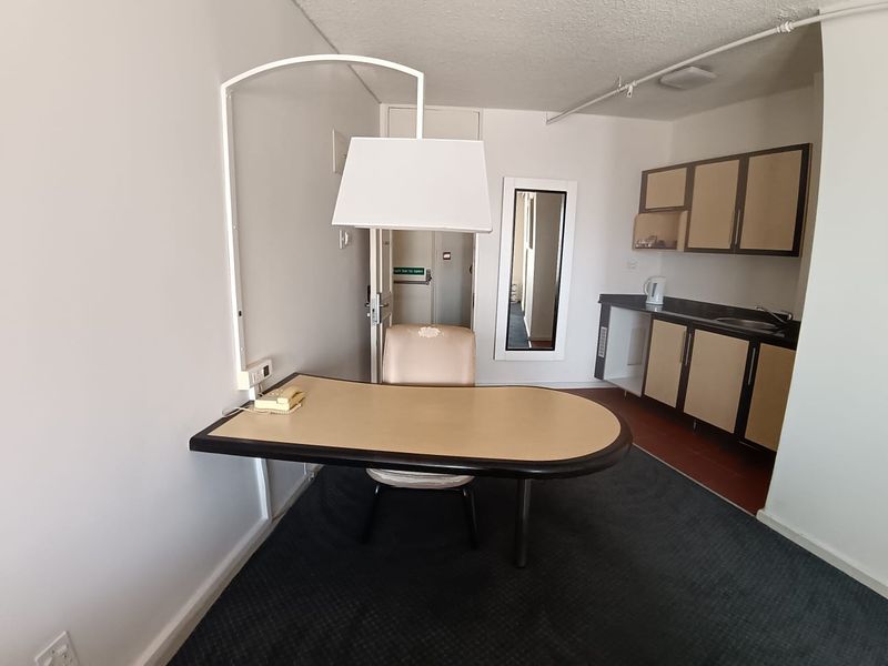 Open plan studio apartment featuring a built-in desk area and a compact kitchenette with basic cabinetry and sink.