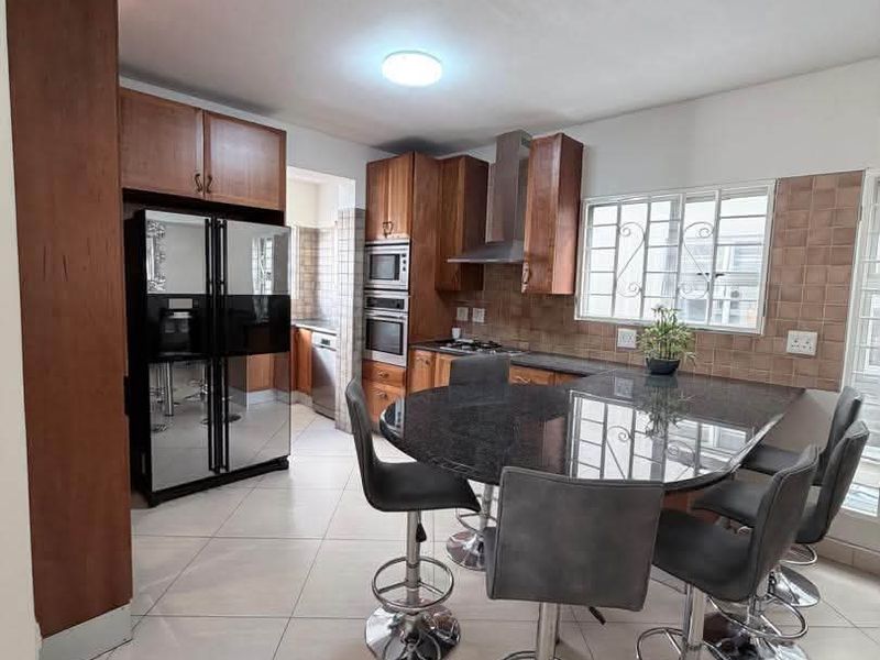 A functional kitchen featuring wooden cabinetry, granite countertops, built-in oven, extractor fan, and tiled flooring with an integrated breakfast bar area.