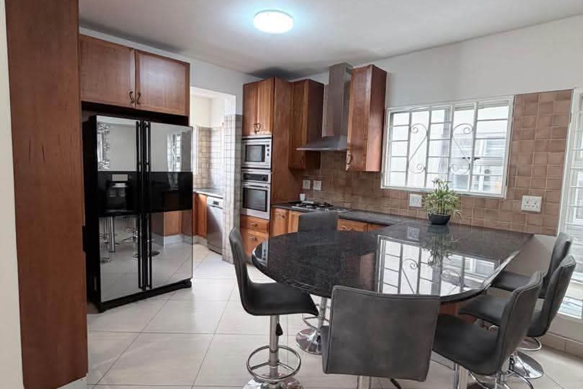 A functional kitchen featuring wooden cabinetry, granite countertops, built-in oven, extractor fan, and tiled flooring with an integrated breakfast bar area.
