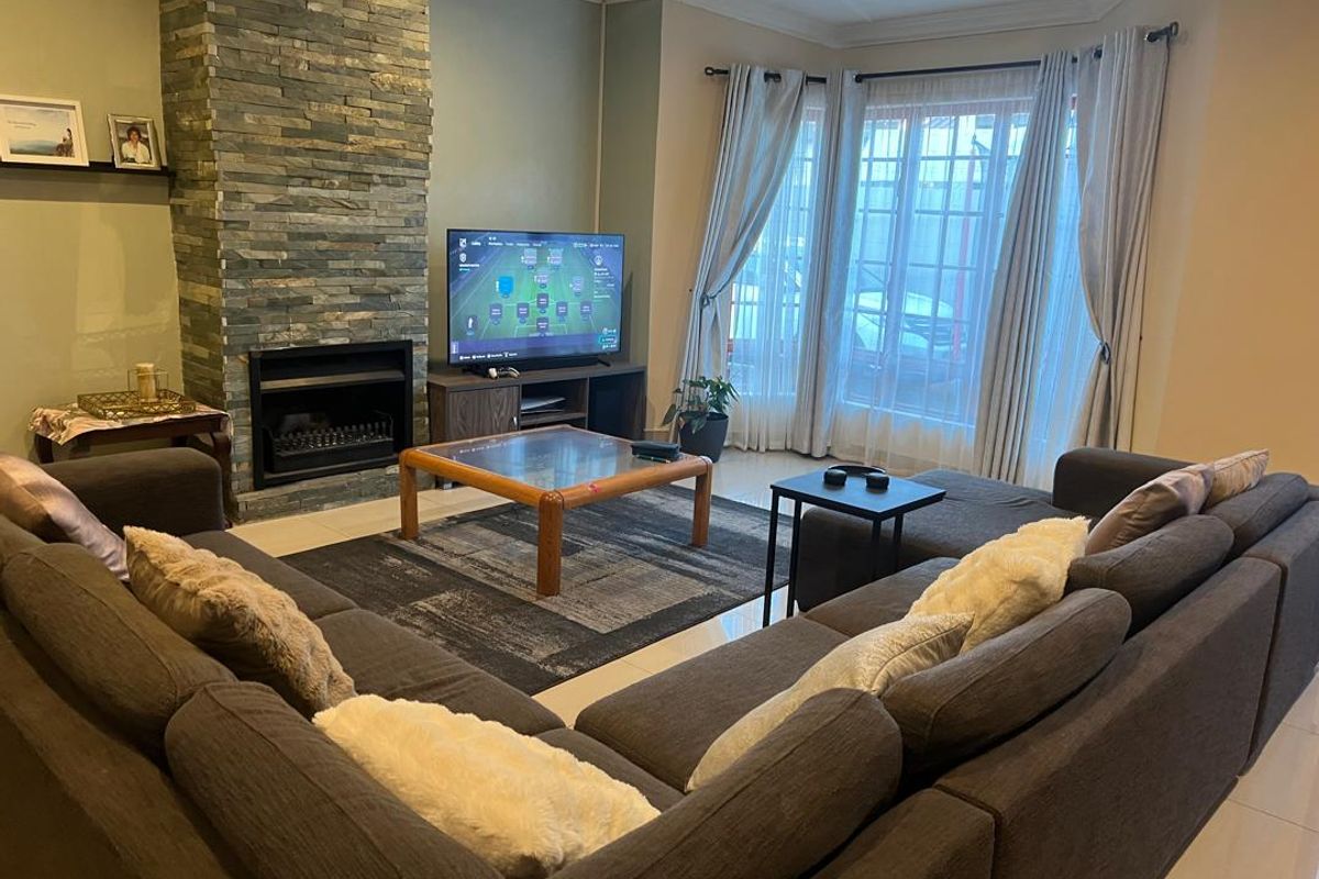 A comfortable living room featuring a prominent stone-clad fireplace, tiled flooring, and large windows that provide ample natural light.