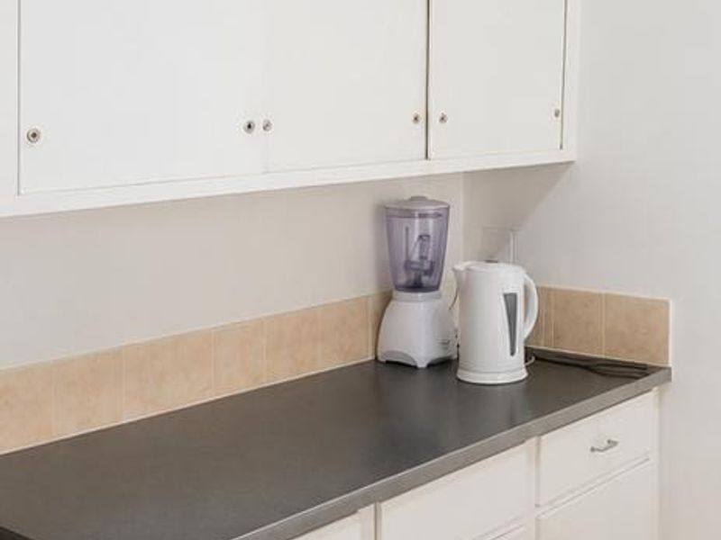 A functional kitchen area featuring white built-in cabinetry, a dark laminate countertop, and neutral tiled backsplash and flooring.