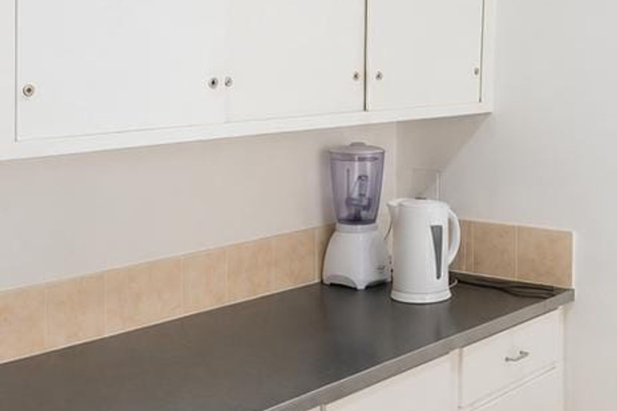 A functional kitchen area featuring white built-in cabinetry, a dark laminate countertop, and neutral tiled backsplash and flooring.
