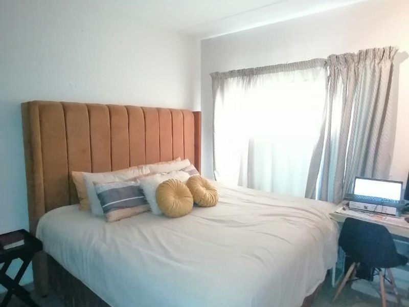A bedroom featuring tiled flooring and track lighting, offering a functional space with natural light from the window.
