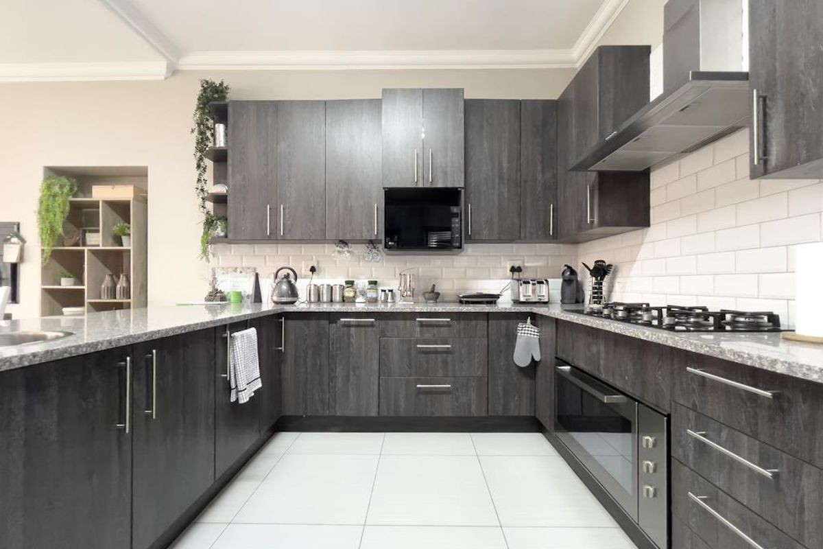 Modern U-shaped kitchen featuring dark wood-grain cabinetry, granite countertops, subway tile backsplash, built-in oven, gas hob, and stainless steel extractor fan.