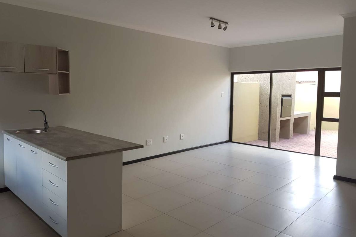 Open-plan living area featuring a modern kitchen island with sink, tiled floors, and direct access to a private patio with a built-in braai.