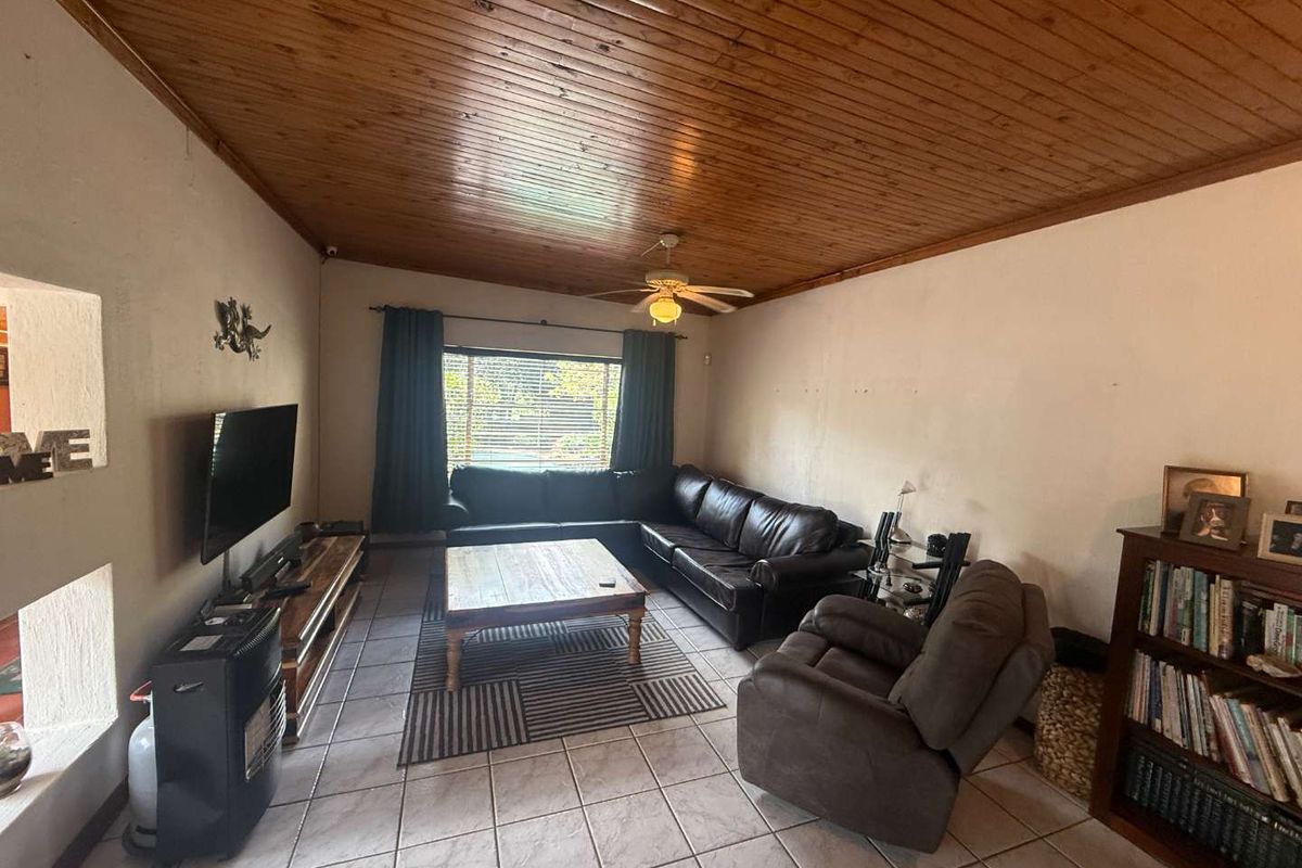 A living room featuring a timber tongue and groove ceiling, ceramic tiled flooring, and a ceiling fan, offering a functional space for relaxation.