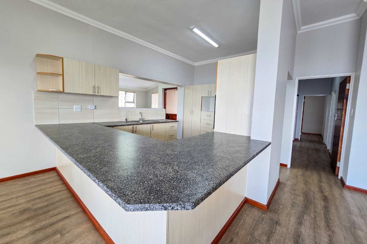 A functional kitchen featuring light wood cabinetry, granite-look laminate countertops, and durable wood-look flooring, offering an open-plan layout with a breakfast bar.