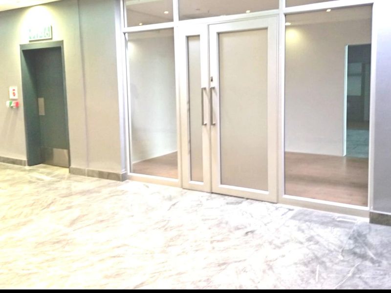 A modern, empty office space featuring marble flooring, glass partitions, and double glass doors, providing a professional and bright working environment.