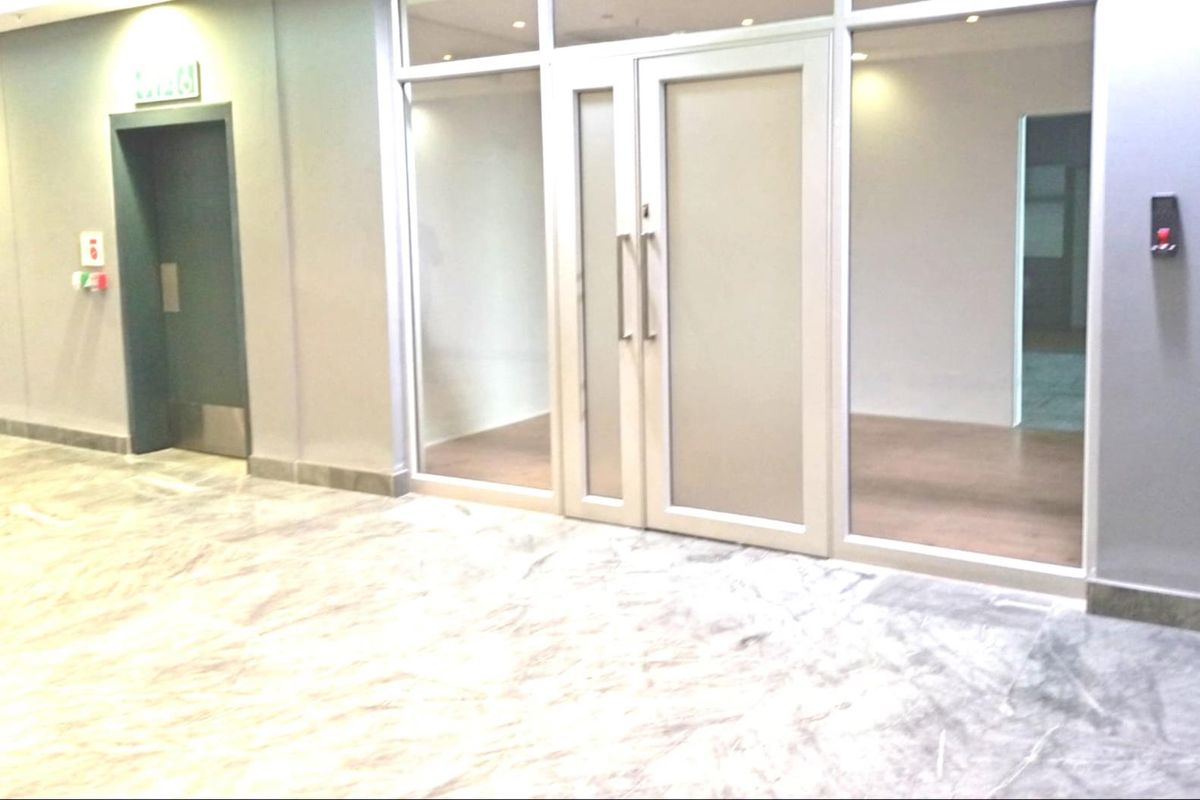 A modern, empty office space featuring marble flooring, glass partitions, and double glass doors, providing a professional and bright working environment.