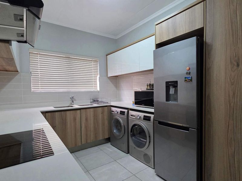 Modern kitchen featuring sleek wood-veneer cabinetry, quartz countertops, integrated appliances, and a clean tiled backsplash, offering a functional and contemporary cooking space.