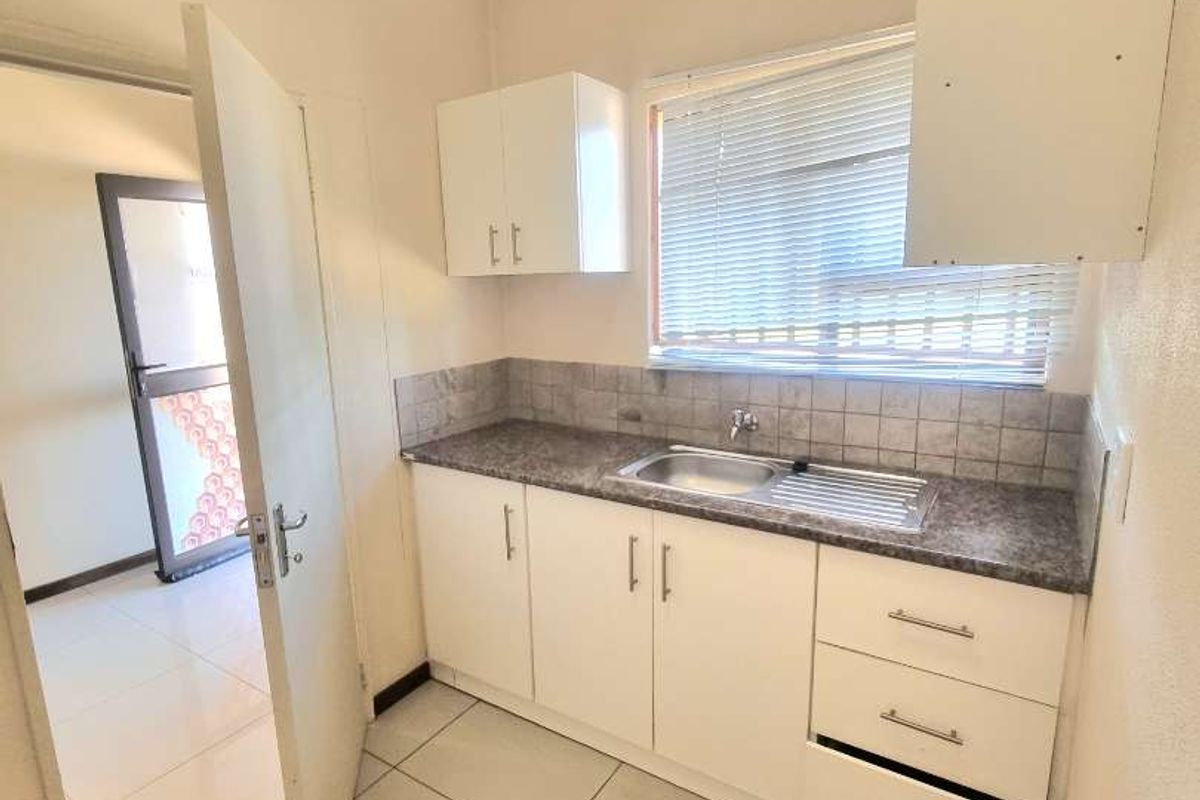 A compact kitchen area featuring white cabinetry, a stainless steel sink, tiled backsplash, and ceramic floor tiles.