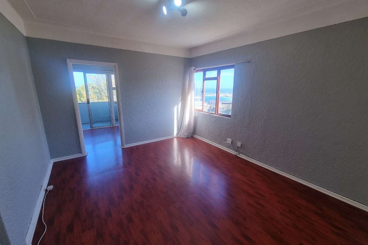 An empty living room featuring laminate flooring, textured walls, and a window with a view, leading to an adjacent balcony area.