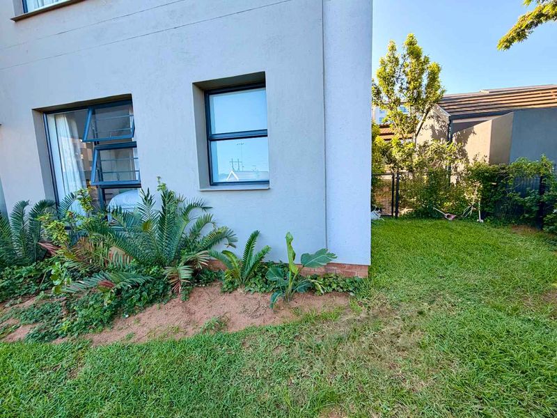 A view of the rear exterior of the apartment, featuring a well-maintained garden, lawn area, and modern aluminium window frames.