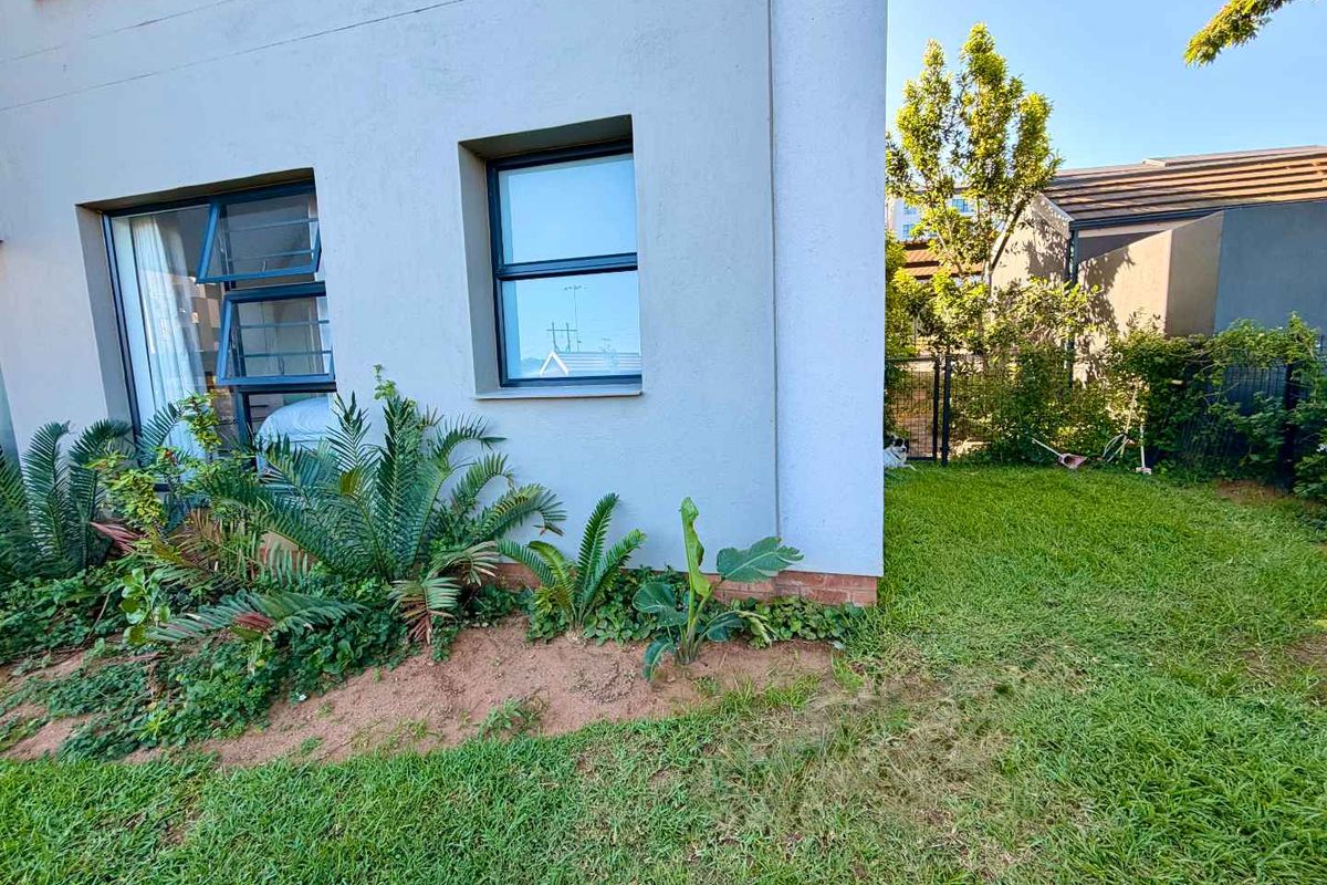 A view of the rear exterior of the apartment, featuring a well-maintained garden, lawn area, and modern aluminium window frames.