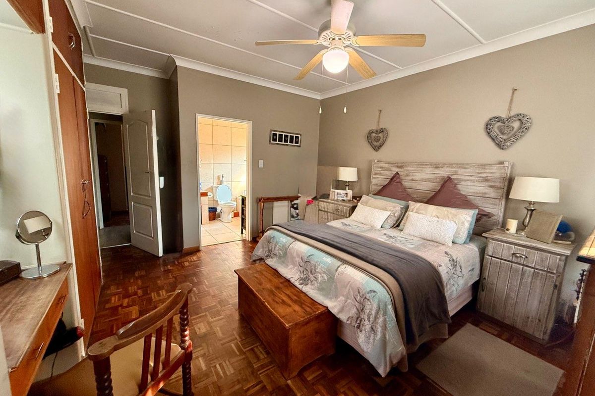 Spacious bedroom featuring parquet flooring, built-in wooden cabinetry, a ceiling fan, and an adjoining en-suite bathroom.