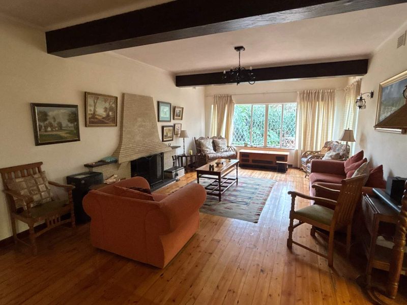 Spacious living room featuring warm timber flooring, exposed ceiling beams, and a classic brick fireplace, offering a comfortable and inviting atmosphere.