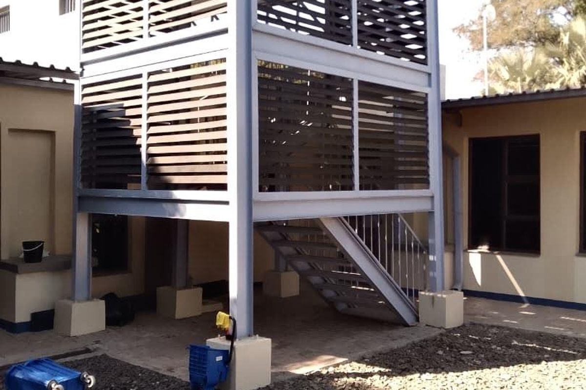 A two-story steel structure featuring an external staircase and louvred privacy screening, situated in a gravel-surfaced rear courtyard area.