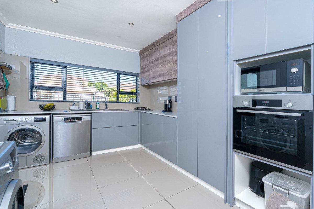 Modern kitchen featuring sleek grey cabinetry, integrated oven and microwave, tiled flooring, and a large window with fitted blinds.