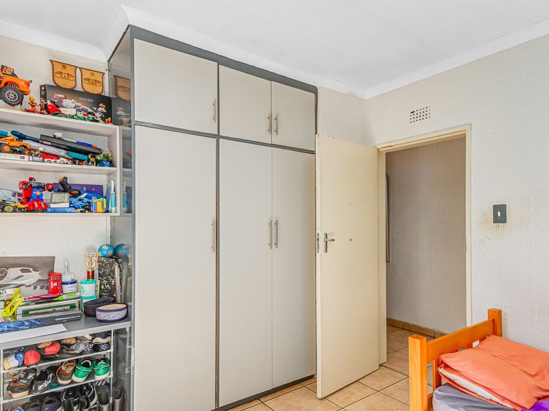 A bedroom featuring built-in cupboards, tiled flooring, and a coved ceiling, providing functional storage and a neutral base for interior updates.