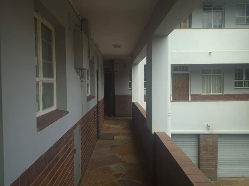An exterior apartment hallway featuring stone flooring, brick accents, and access to building stairwells and unit entrances.
