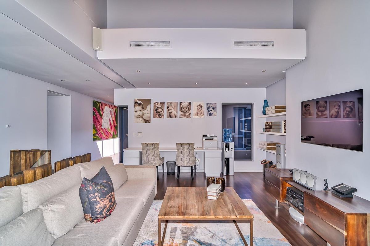 A modern living room featuring high ceilings, recessed lighting, integrated ducted air conditioning, and a built-in workspace with shelving.