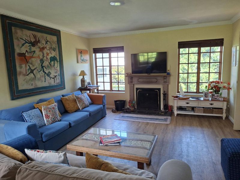 A comfortable living room featuring a central fireplace with a mantelpiece, laminate flooring, crown molding, and large windows providing natural light.