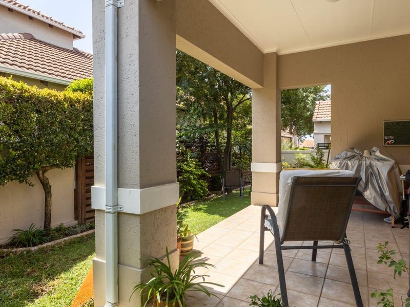 A covered patio area featuring tiled flooring and concrete pillars, overlooking a private garden space.