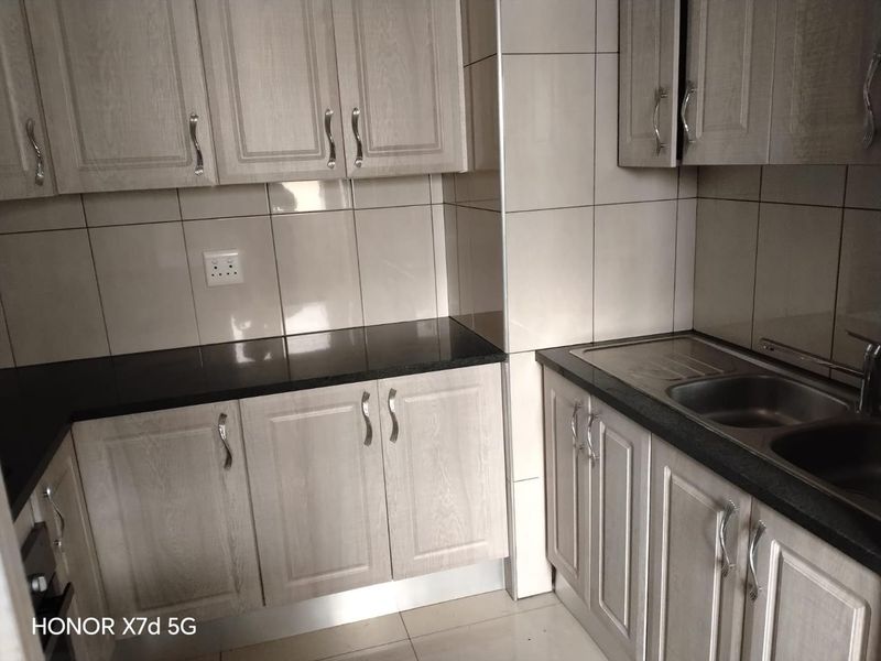 A clean, modern kitchen featuring light wood-grain cabinetry, dark granite countertops, and a stainless steel sink with a tiled backsplash.