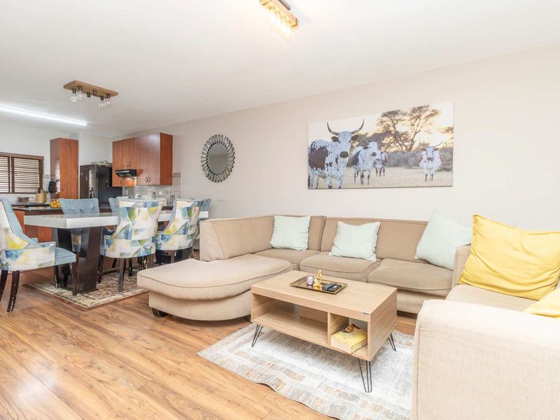 An open-plan living and dining area featuring laminate flooring, neutral walls, and a functional kitchen with wood-finish cabinetry and integrated appliances.