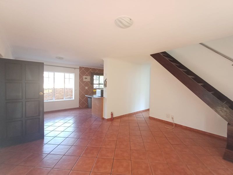 Open plan living area featuring tiled flooring and a wooden staircase leading to the upper level, with an adjacent kitchen counter area.