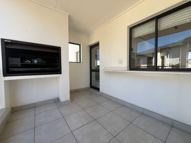 A clean, covered patio area featuring a built-in braai, tiled flooring, and a convenient serving counter, perfect for outdoor entertaining.