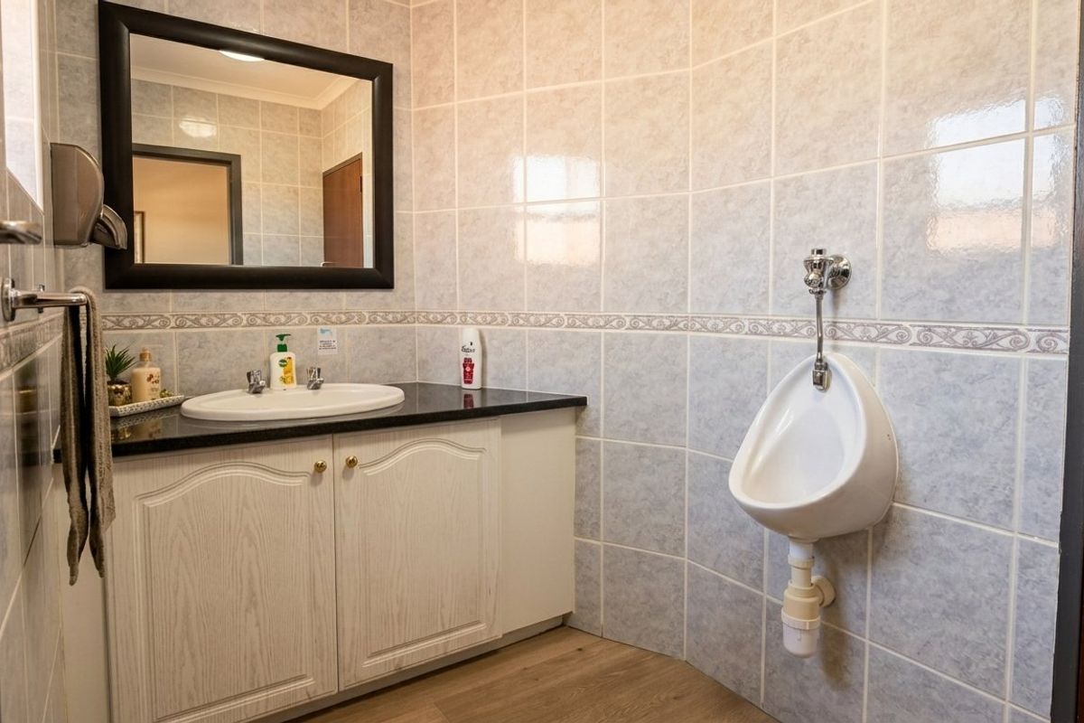 A functional commercial bathroom featuring a vanity with a washbasin, a wall-mounted urinal, and tiled wall finishes.