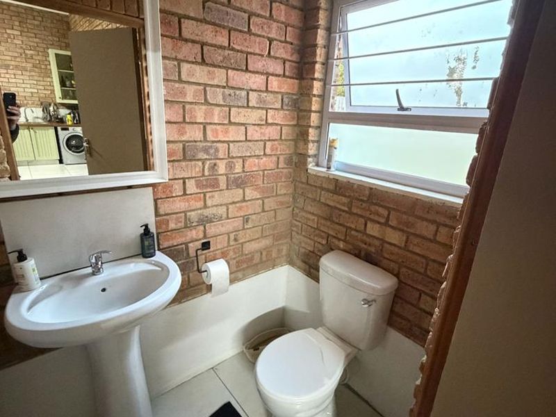 Compact bathroom featuring exposed brick walls, a pedestal basin, and a standard toilet with a top-hung window for natural light.