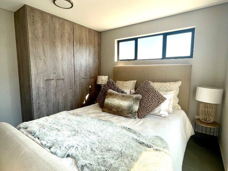 A well-maintained bedroom featuring built-in wooden cupboards, modern recessed ceiling lighting, and a horizontal window providing natural light.
